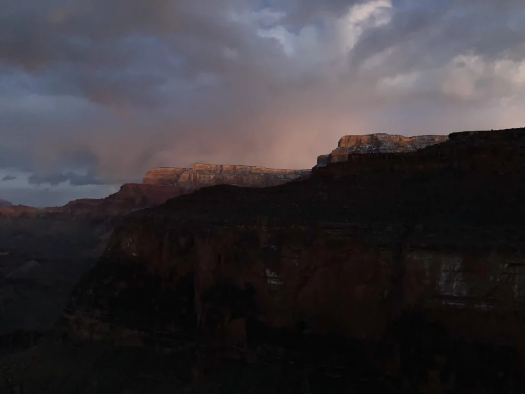 sunset in the Grand Canyon, with a dark ridgeline and cloudy sky with lots of color