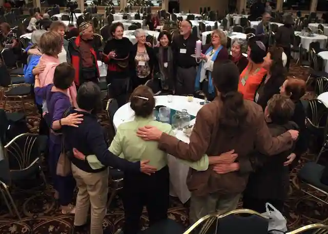 spiritual companions at a conference, gathered around tables, arms around each other, experiencing spiritual community